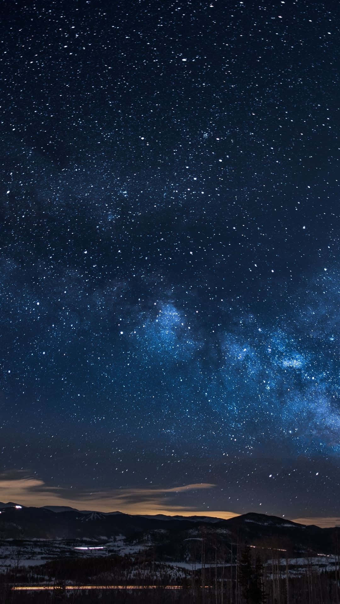 星空 桌布 壁紙 — 令人嘆為觀止的夜空，佈滿無數星星，閃爍的銀河在積雪的山脈和遠處的小鎮上空拱起。
