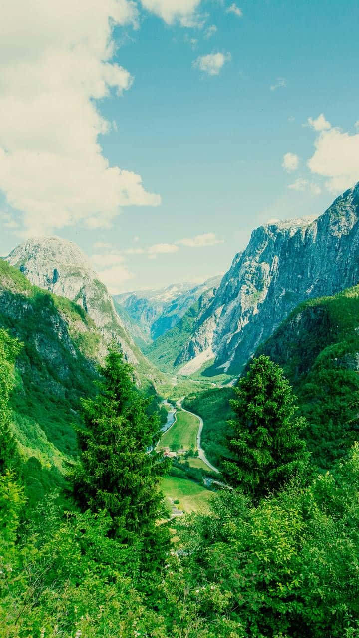 Valley 桌布 壁紙 — 令人嘆為觀止的景色，鬱鬱蔥蔥的綠色山谷坐落在高聳的岩石山脈之間，在明亮的藍天下有蓬鬆的白雲。