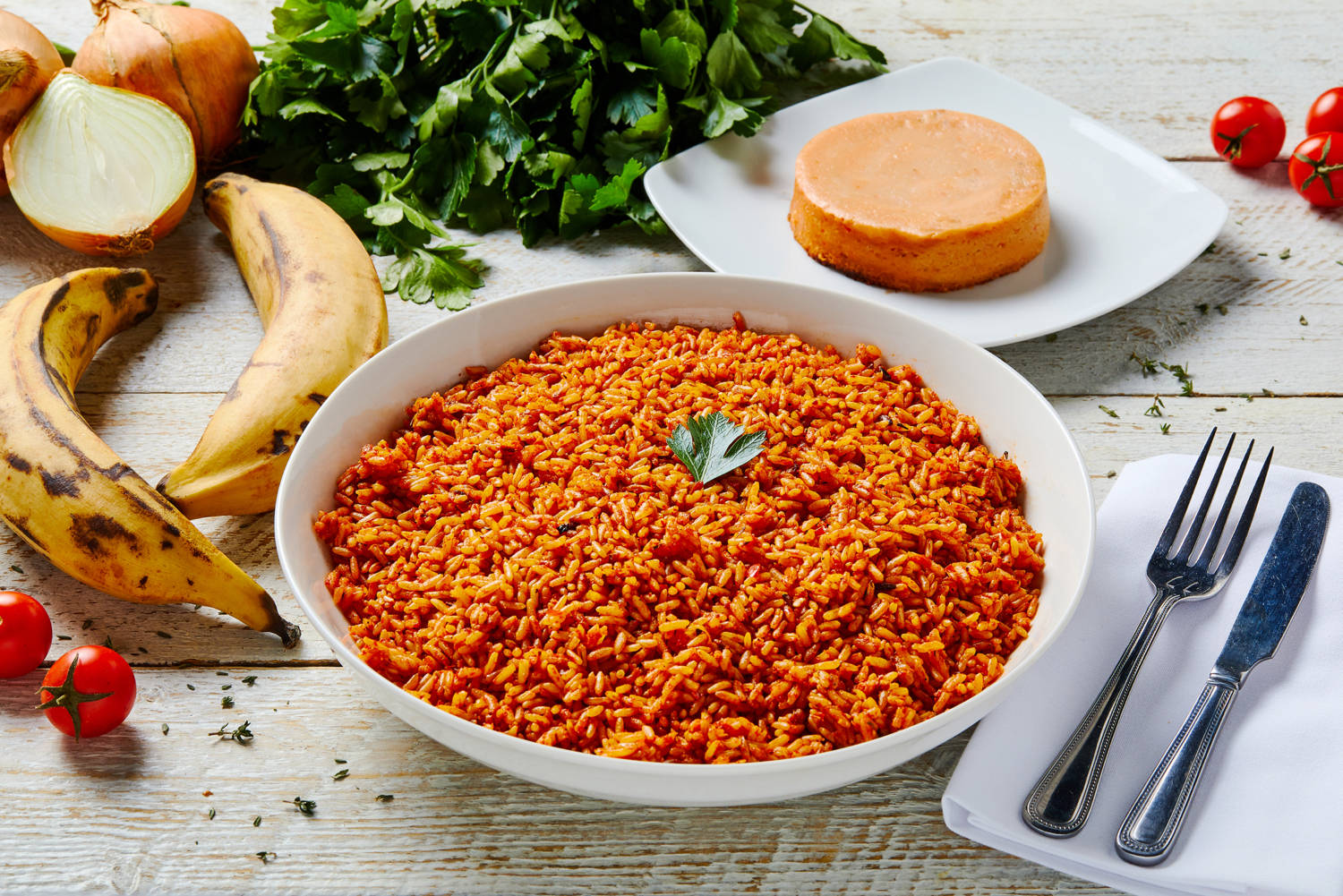 令人垂涎的約洛夫飯 完美餐點 壁紙 — 一碗色彩鮮豔的橙紅色米飯，飾以歐芹，放在質樸的木桌上，旁邊有香蕉、番茄和一個小蛋糕。