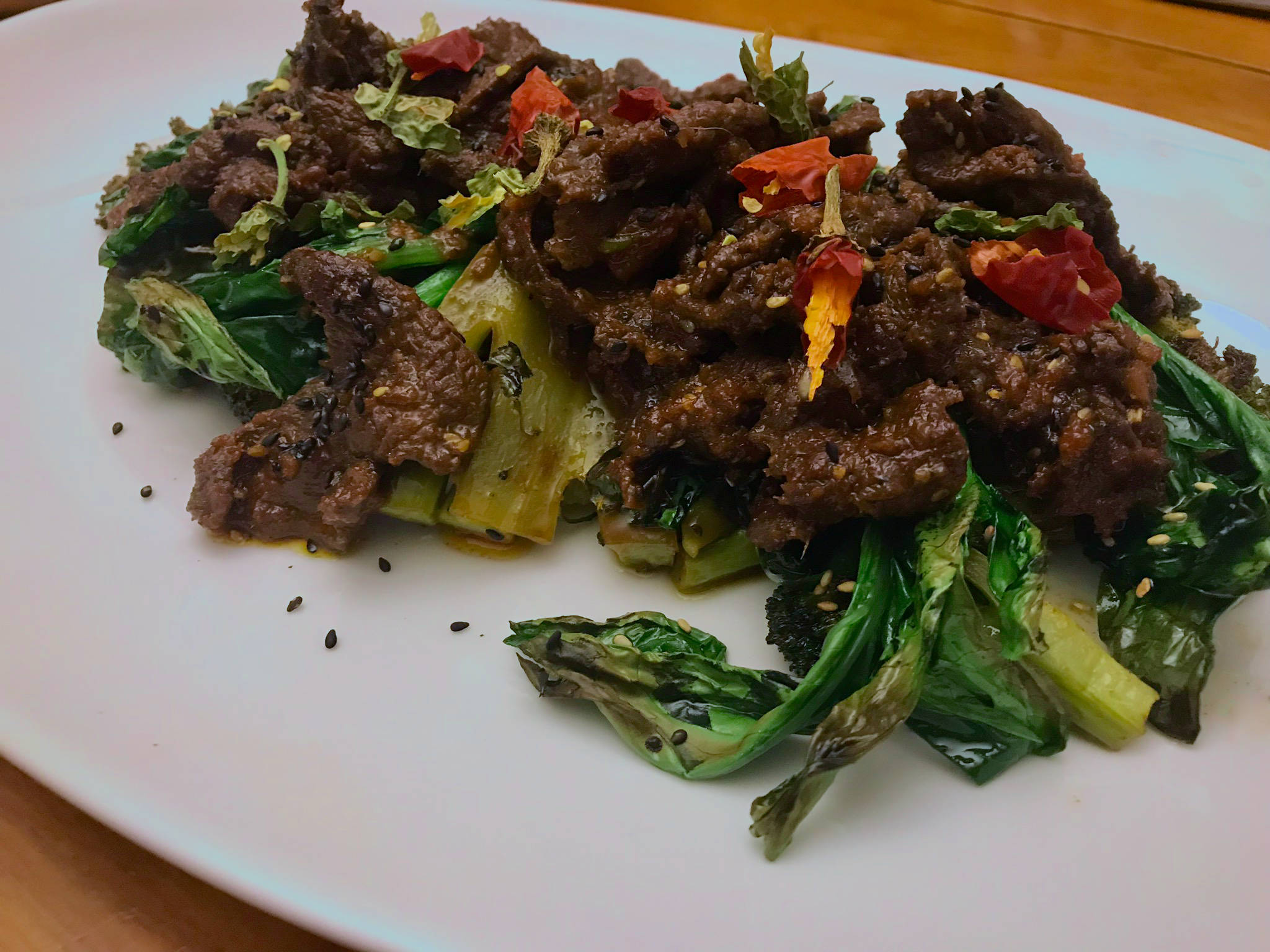 令人垂涎的韓式醬油牛肉——韓國芝麻牛肉 壁紙 — 白色碟上嘅滋滋作響牛肉同烤焦蔬菜，上面放咗紅辣椒同黑芝麻。