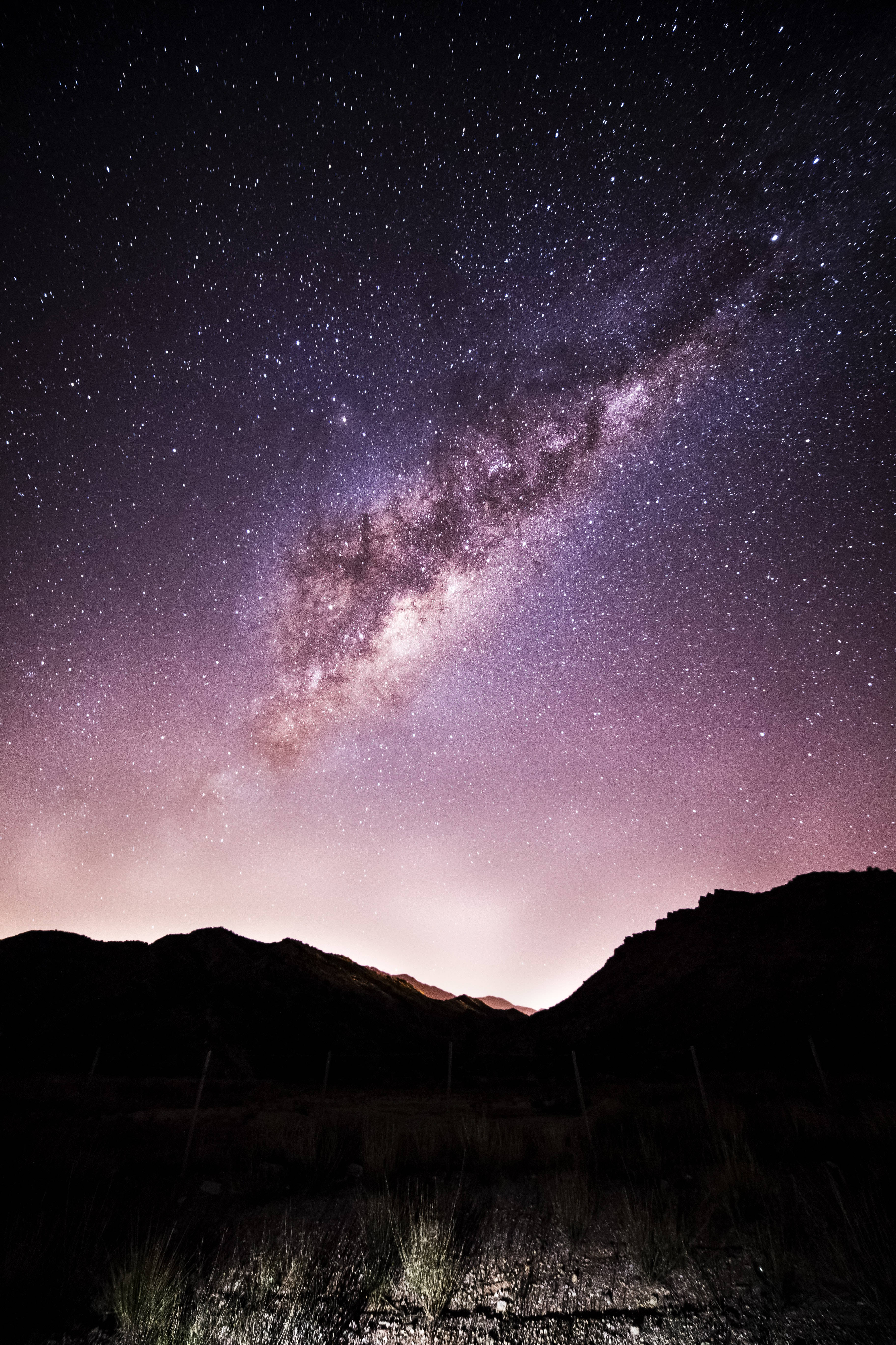 夜空 桌布 壁紙 — 令人屏息的夜空，充滿無數星星，發光的銀河在黑暗的山脈剪影上彎曲。