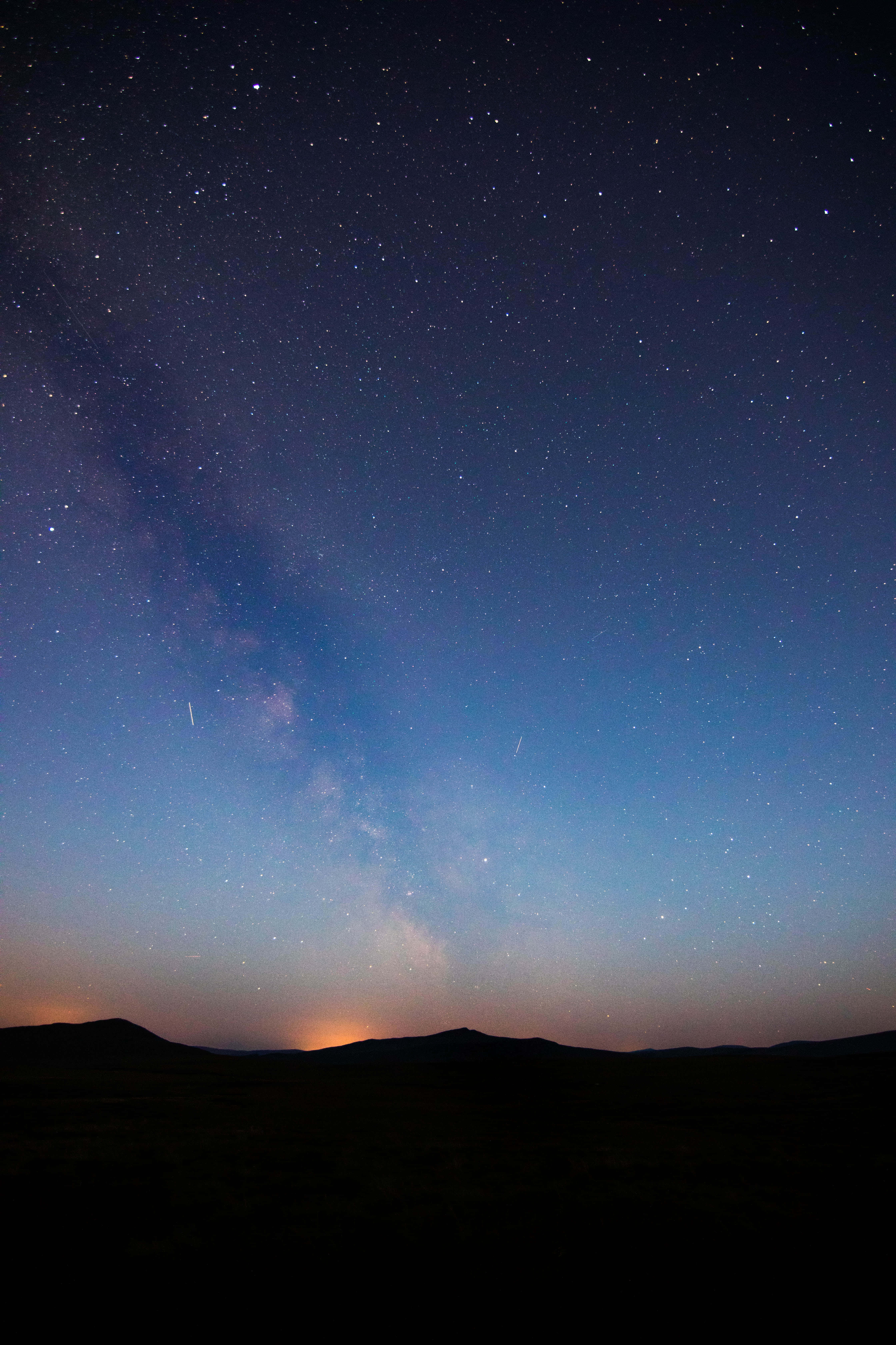 Silhouette 桌布 壁紙 — 令人屏息的夜空佈滿繁星，銀河拱跨在黑暗的輪廓山丘之上，地平線散發溫暖的光芒。