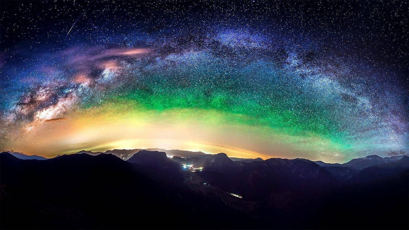 Mountain 桌布 壁紙 — 令人屏息的夜空籠罩著山巒剪影，銀河與北極光以鮮豔的綠色和紫色閃耀。