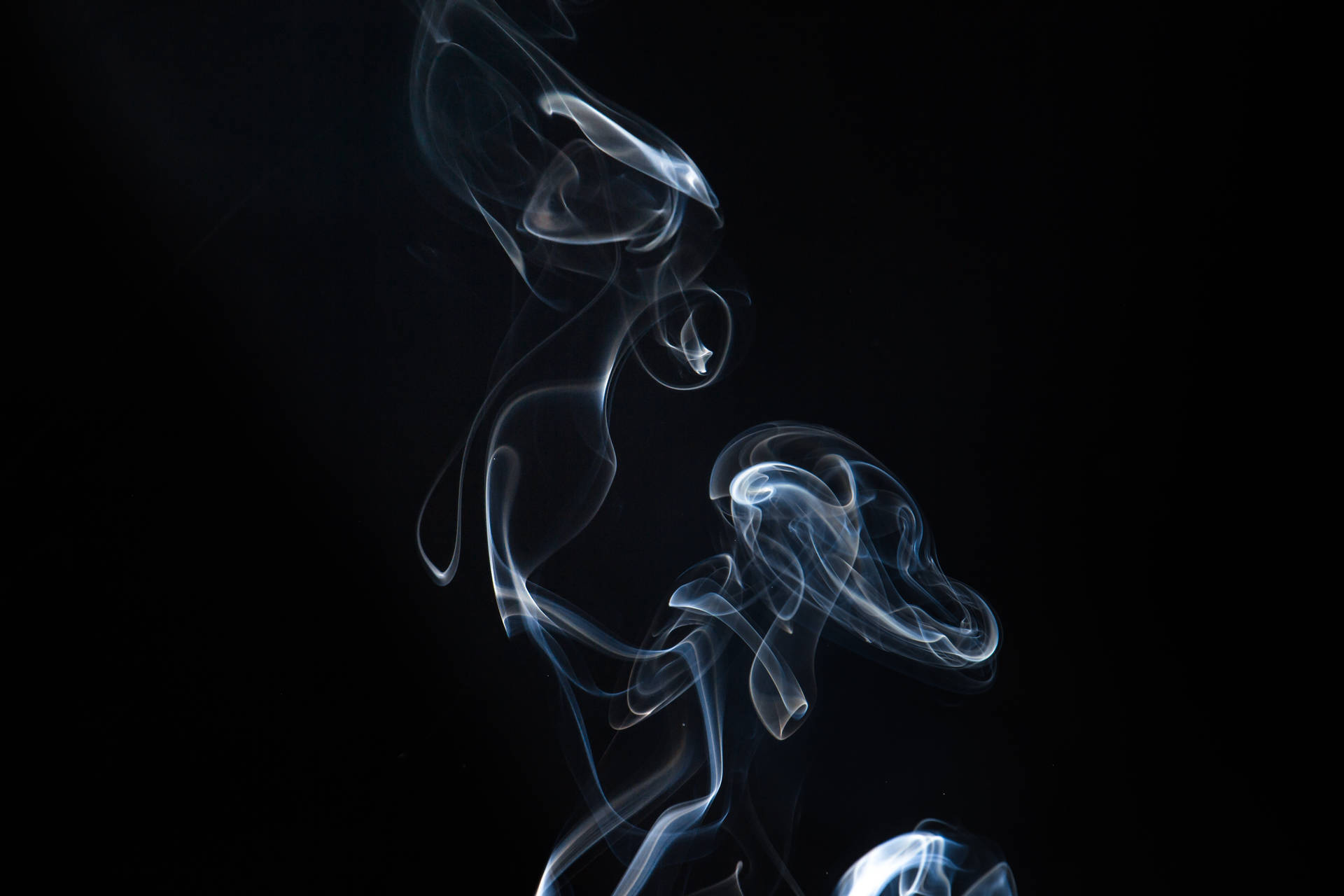 優雅的藍色煙霧漩渦在純黑色背景上昇起。