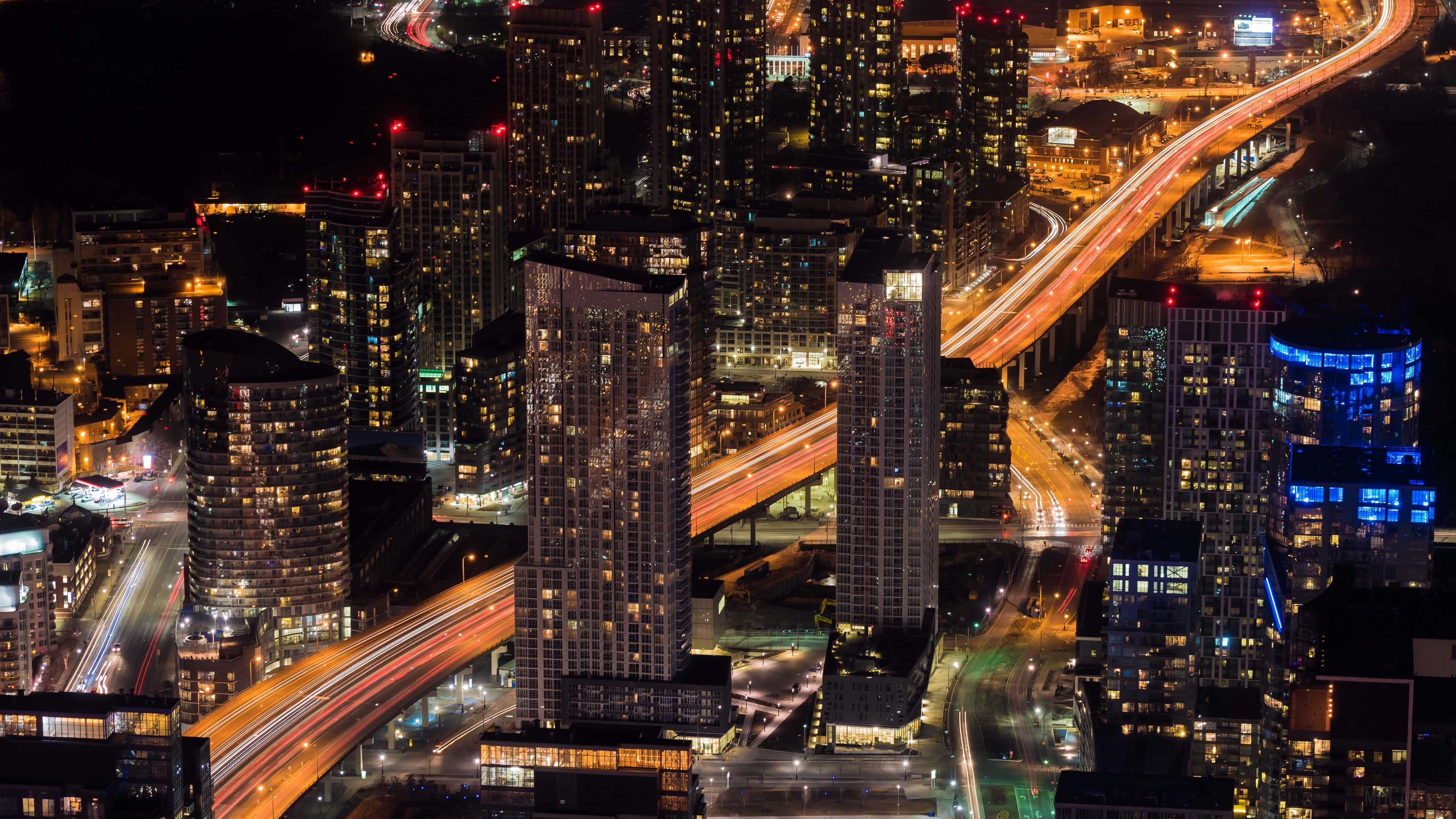 令人屏息的高品質風景照片 壁紙 — 繁忙城市景觀的空中夜景，有發光的摩天大樓和高架高速公路上的車流光跡。