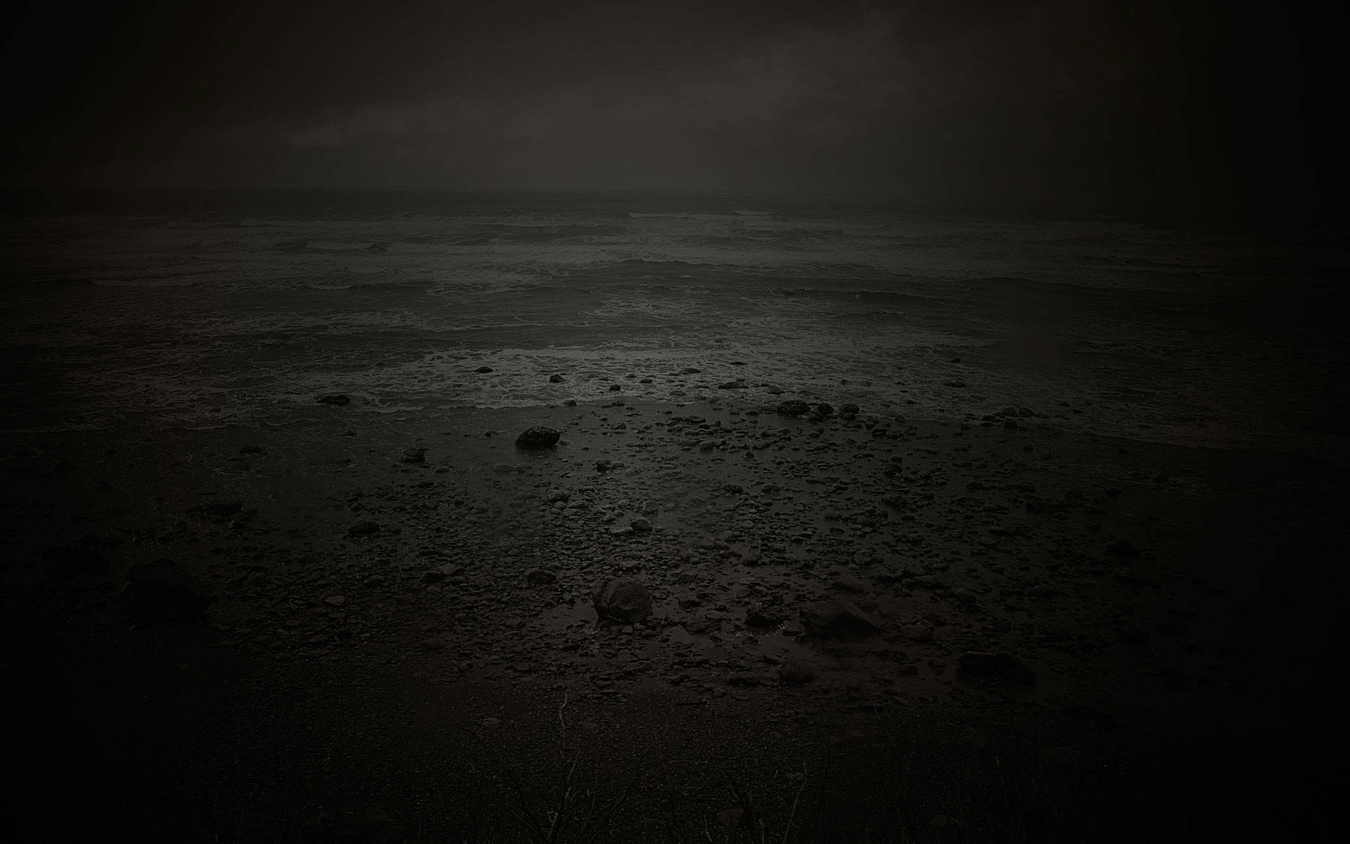 令人沮喪的夜間海灘 壁紙 — 夜晚荒涼陰暗的海灘，濕沙、岩石和幾乎沒有月光照亮的暴風雨天空。