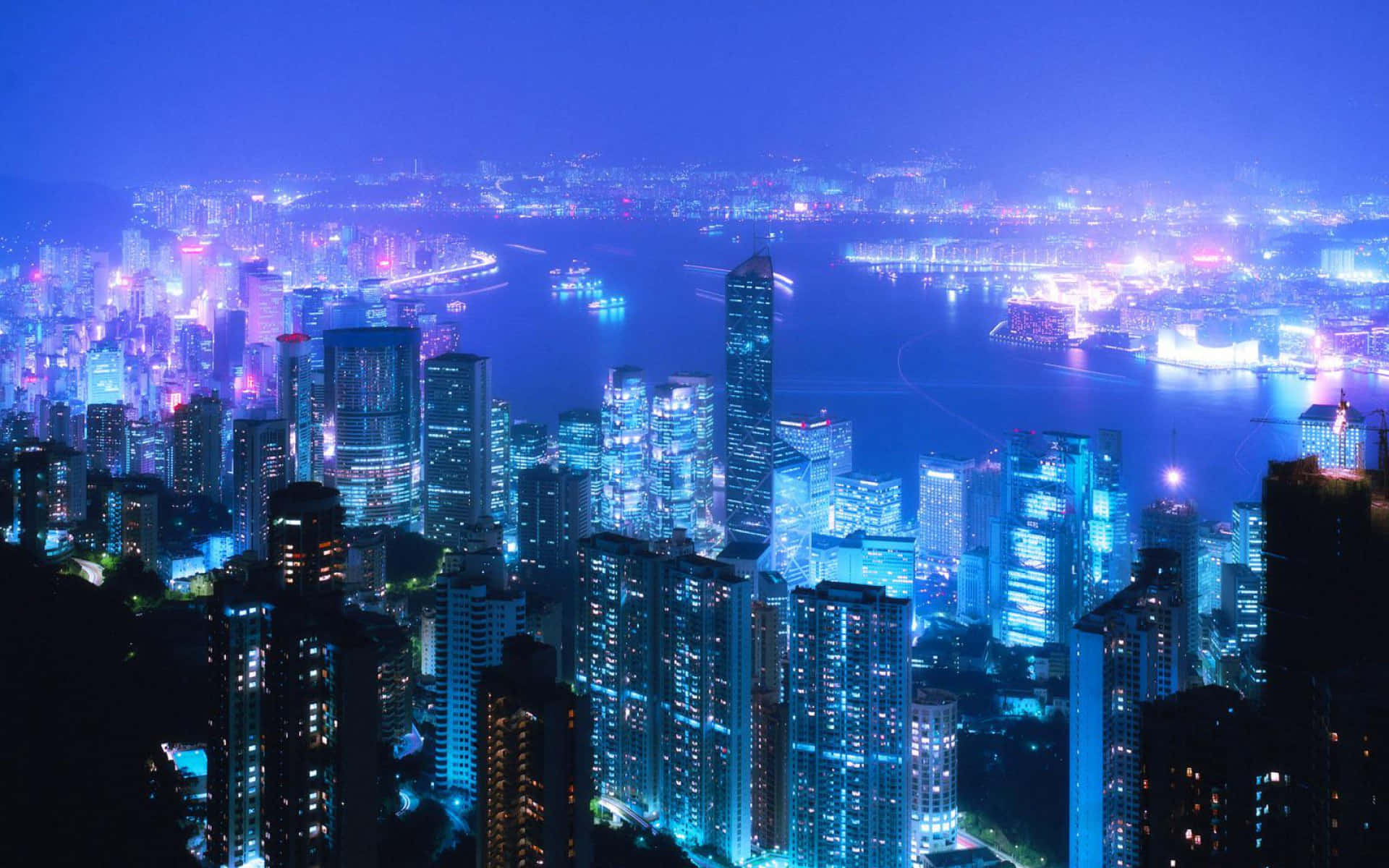 城市景觀 桌布 壁紙 — 令人目眩的夜景，高聳的摩天大樓沿著充滿活力的海濱閃爍著藍色和紫色的燈光。