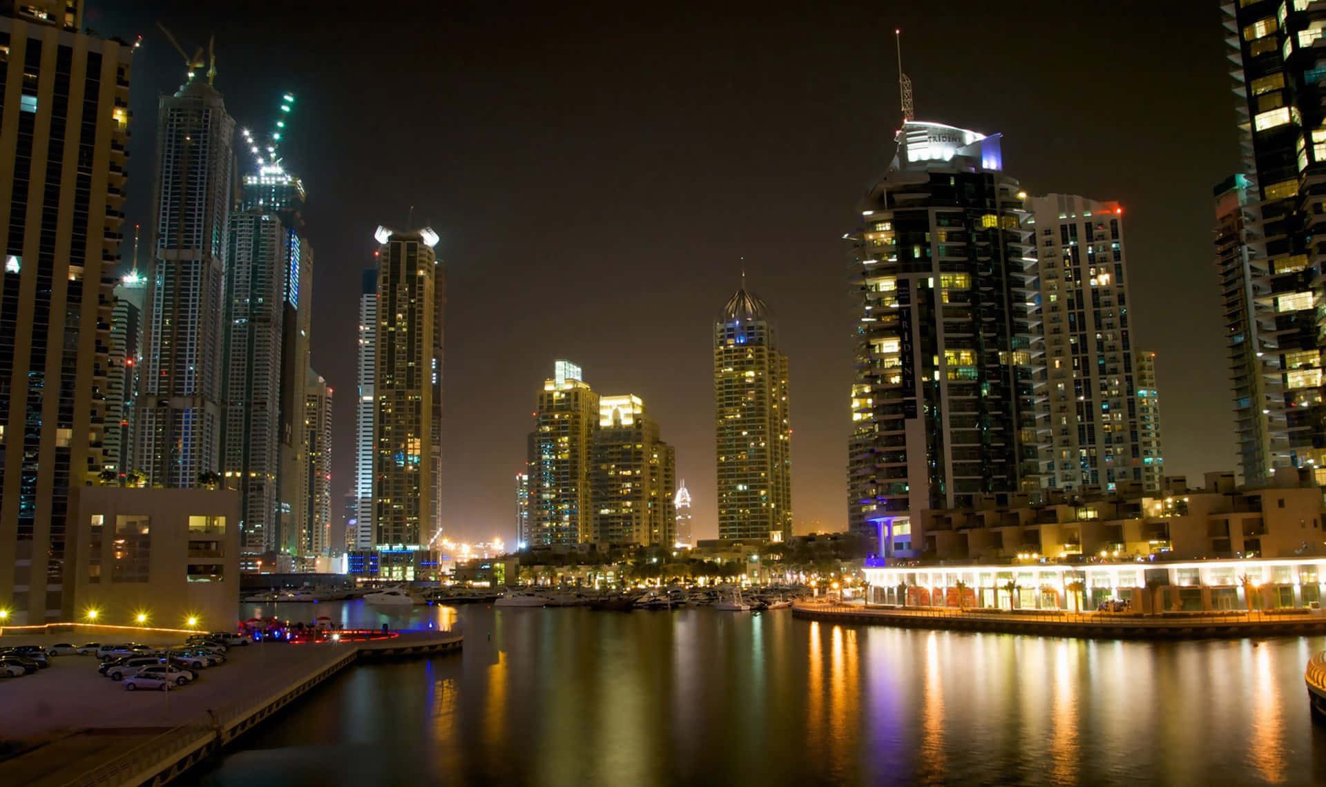 Dubai 桌布 壁紙 — 令人目眩的夜景城市景觀，高聳的摩天大樓在平靜的水面上反射出金色和藍色的燈光。
