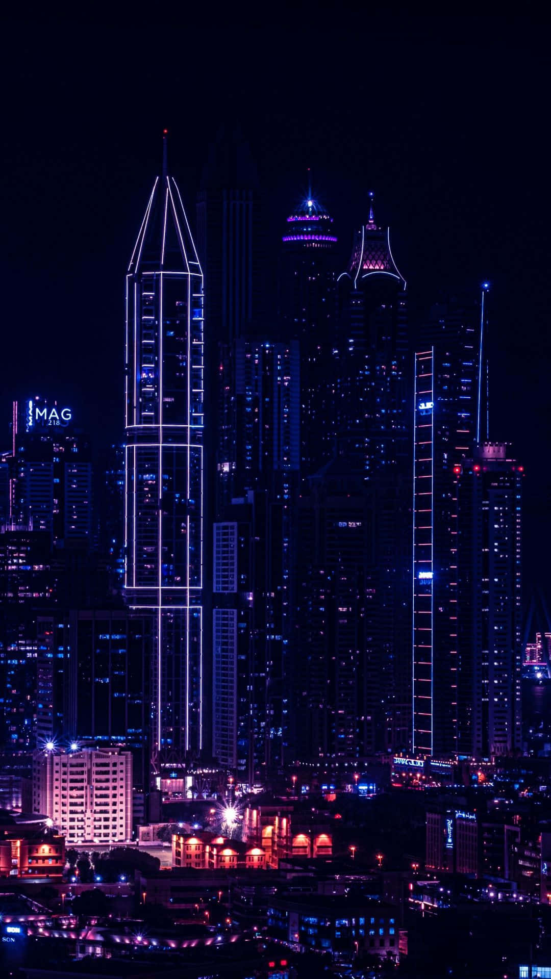 城市景觀 桌布 壁紙 — 令人目眩的夜景城市景觀，高聳的摩天大樓在深黑色的天空映襯下閃耀著電光藍和紫色霓虹燈光。