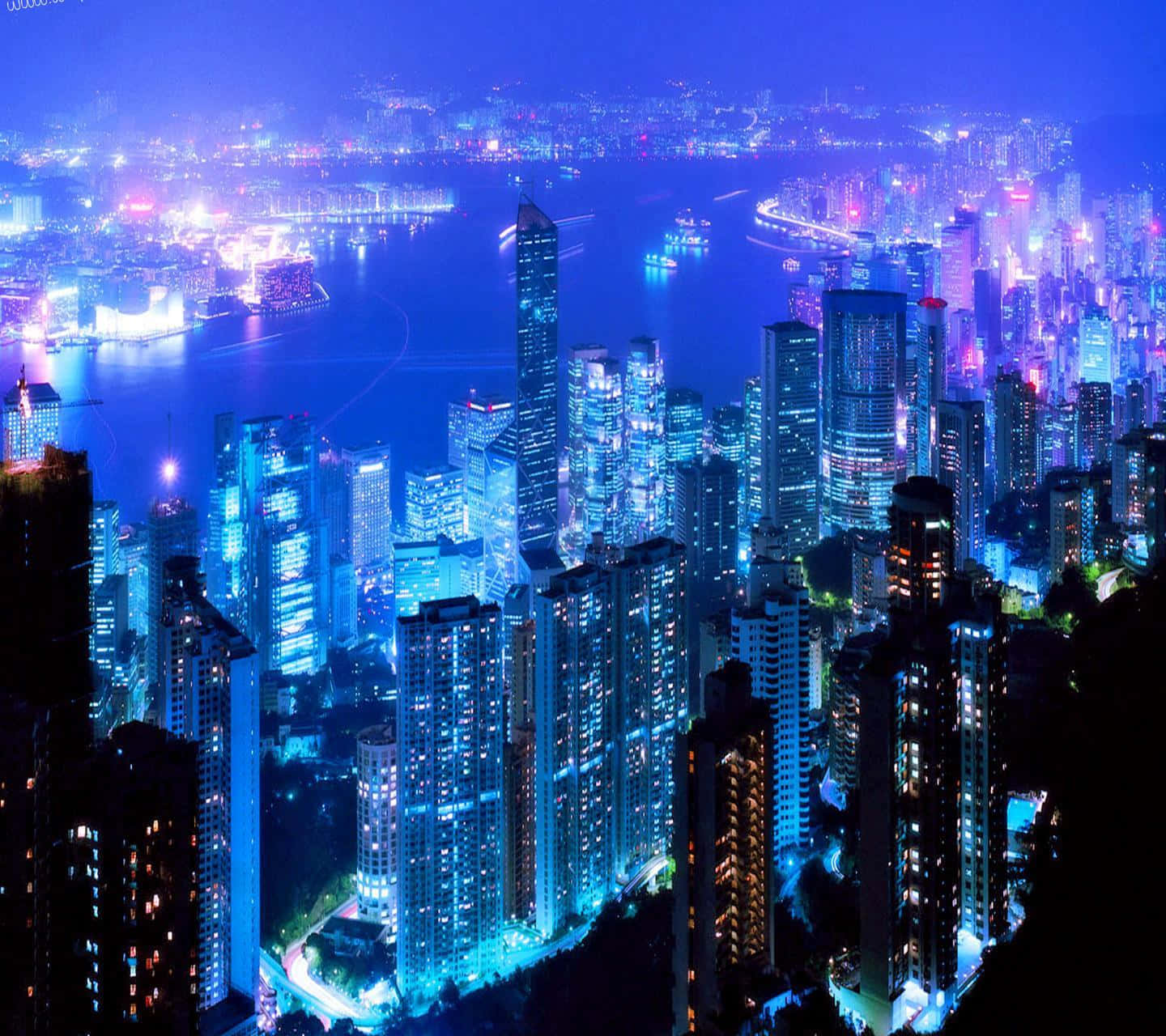 3d City 桌布 壁紙 — 令人眼花繚亂的夜景，高聳的摩天大樓沿著充滿活力的海濱閃爍著藍色和紫色的燈光。