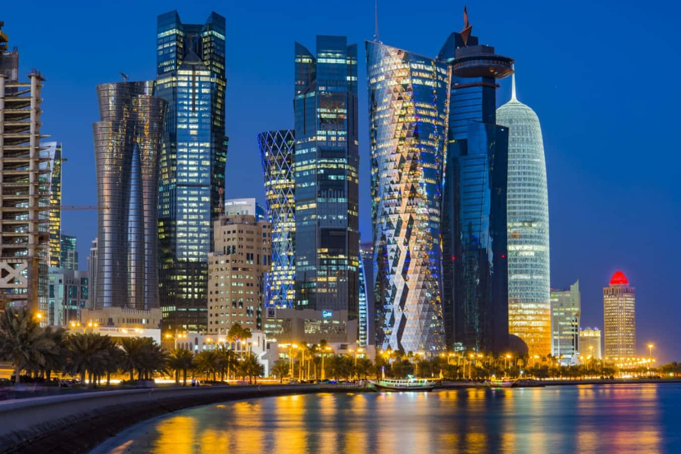 Qatar 桌布 壁紙 — 令人眼花繚亂的未來主義摩天大樓夜景，金色燈光倒映在平靜的水面上，海濱種滿棕櫚樹。