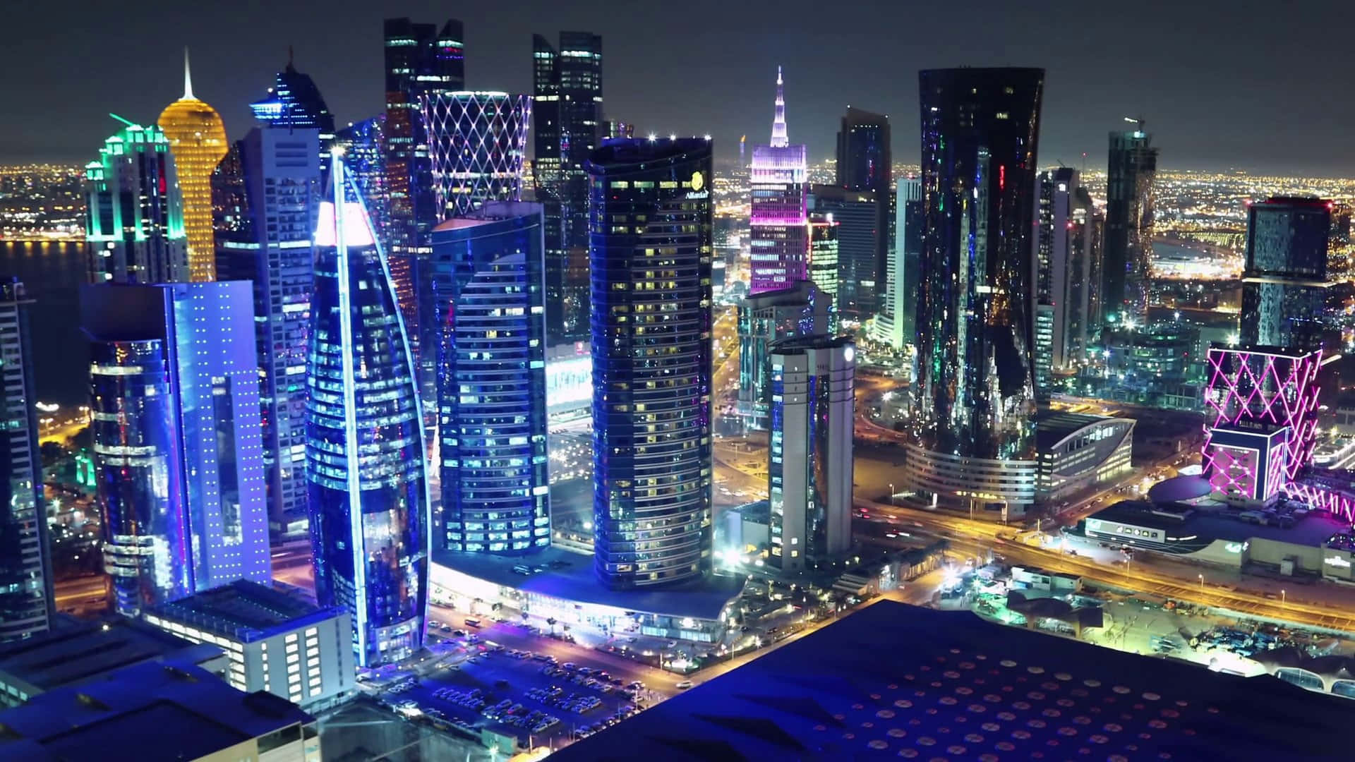 Qatar 桌布 壁紙 — 令人眼花繚亂的未來主義摩天大樓夜景，在黑暗的天空中閃爍著藍色、紫色和金色的光芒。