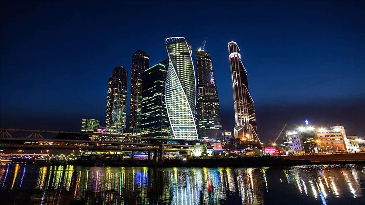 Russia 桌布 壁紙 — 令人眼花繚亂的現代摩天大樓夜景，璀璨燈光倒映在平靜的河面上。