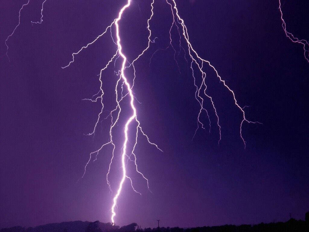強大的閃電照亮了遠處剪影上方的深紫色風暴天空。