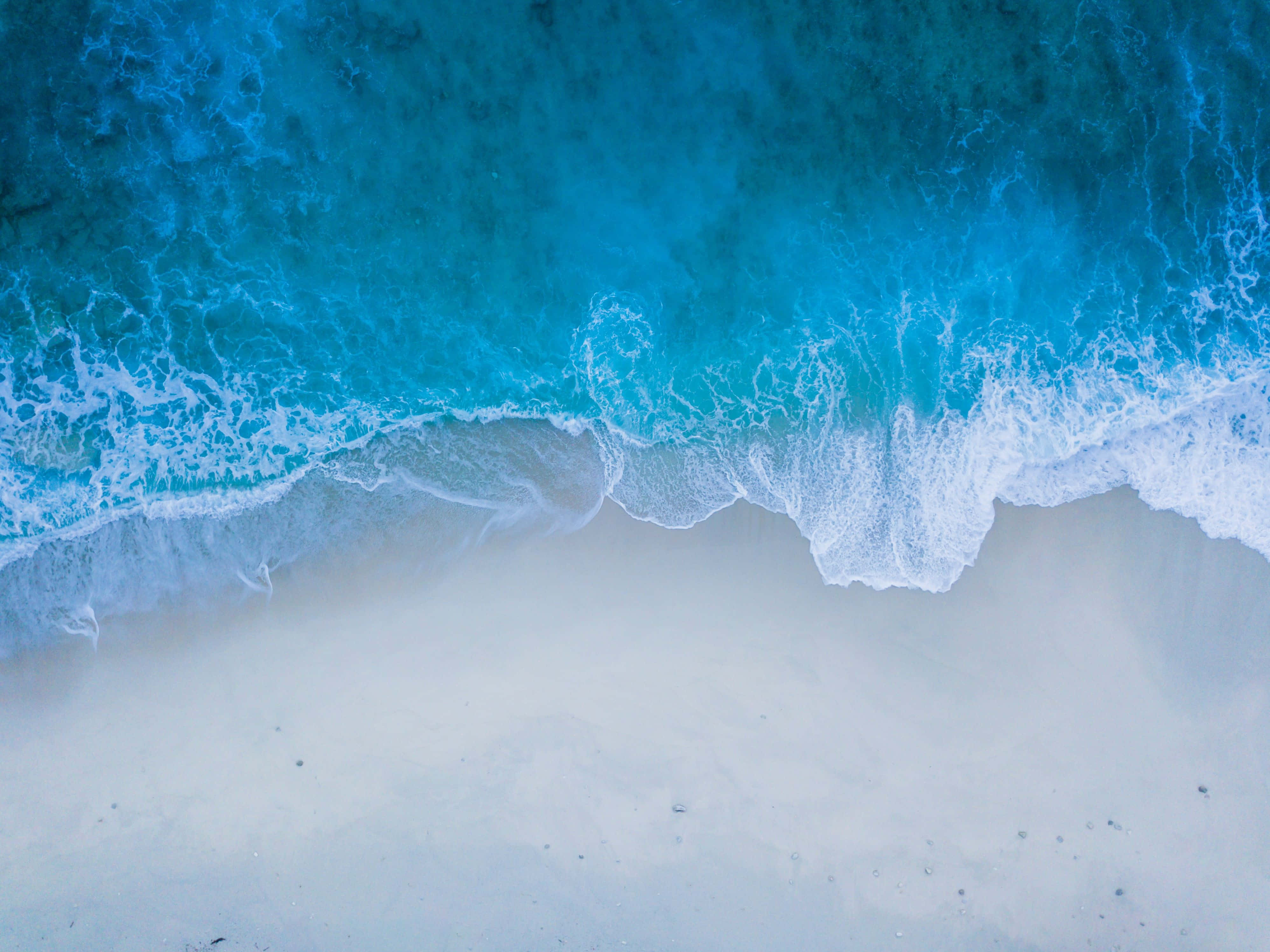 令人著迷的海面日落美景 壁紙 — 從高空俯瞰，碧綠的海浪拍打著純淨的白色沙灘。