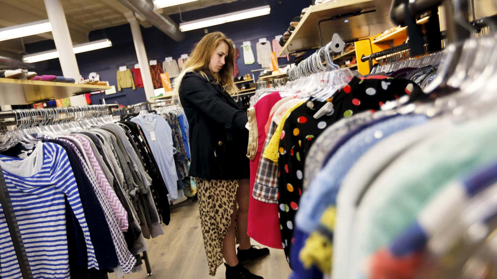 女性在色彩繽紛的二手店通道購物衣服。