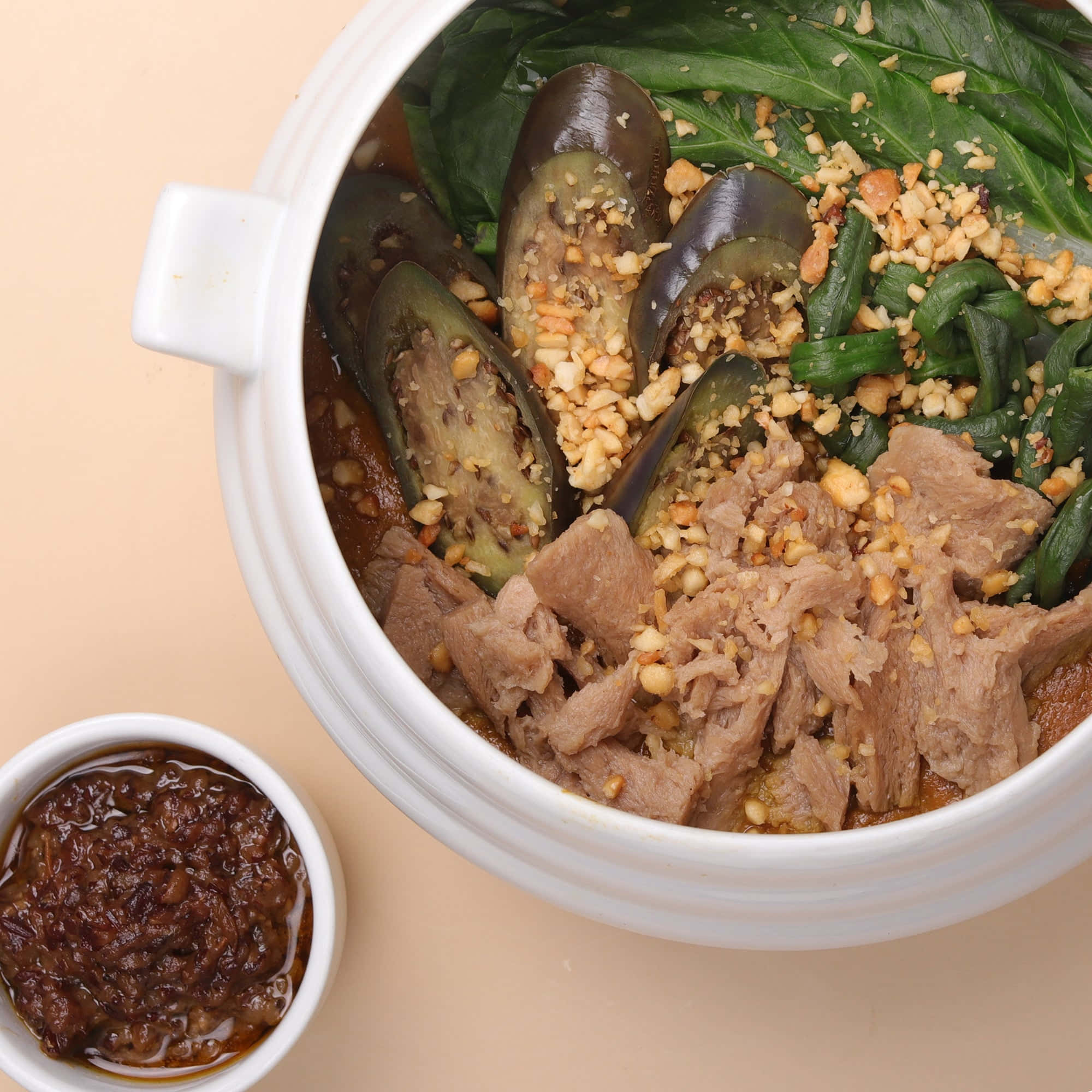 令人食指大動的菲律賓料理——咖喱燉菜 壁紙 — 一個白色陶瓷碗，裝滿嫩肉片、茄子和菠菜，上面撒上碎花生，旁邊配有深色蘸醬。