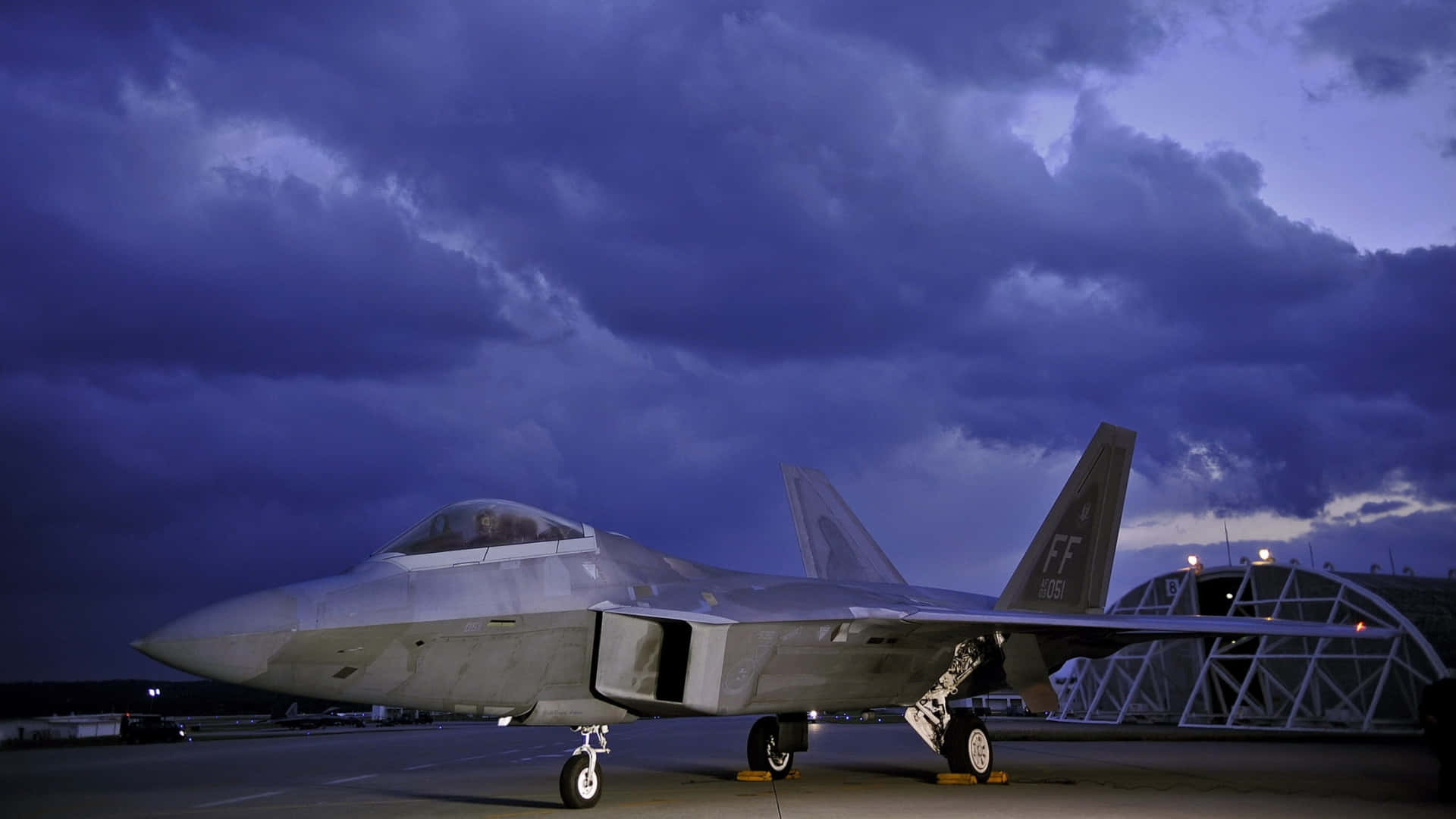 灰色戰鬥機停在停機坪上，紫色暮色天空有雲。