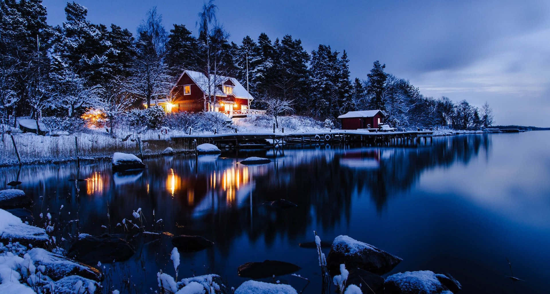 夜間水邊的雪地小屋，溫暖燈光倒映在平靜水面