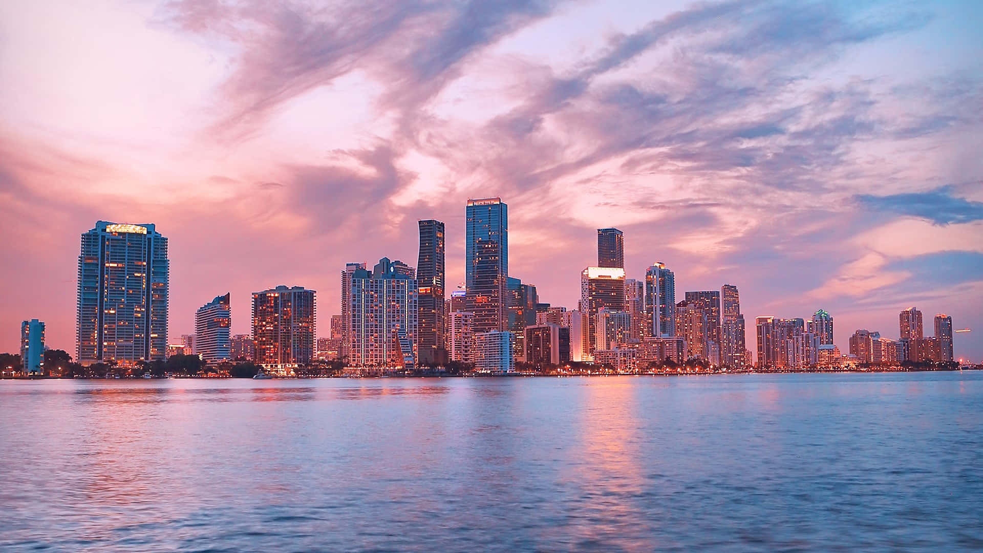 Miami 桌布 壁紙 — 令人驚嘆的城市天際線在日落時分，粉紅色和紫色的雲彩倒映在平靜的水面上。