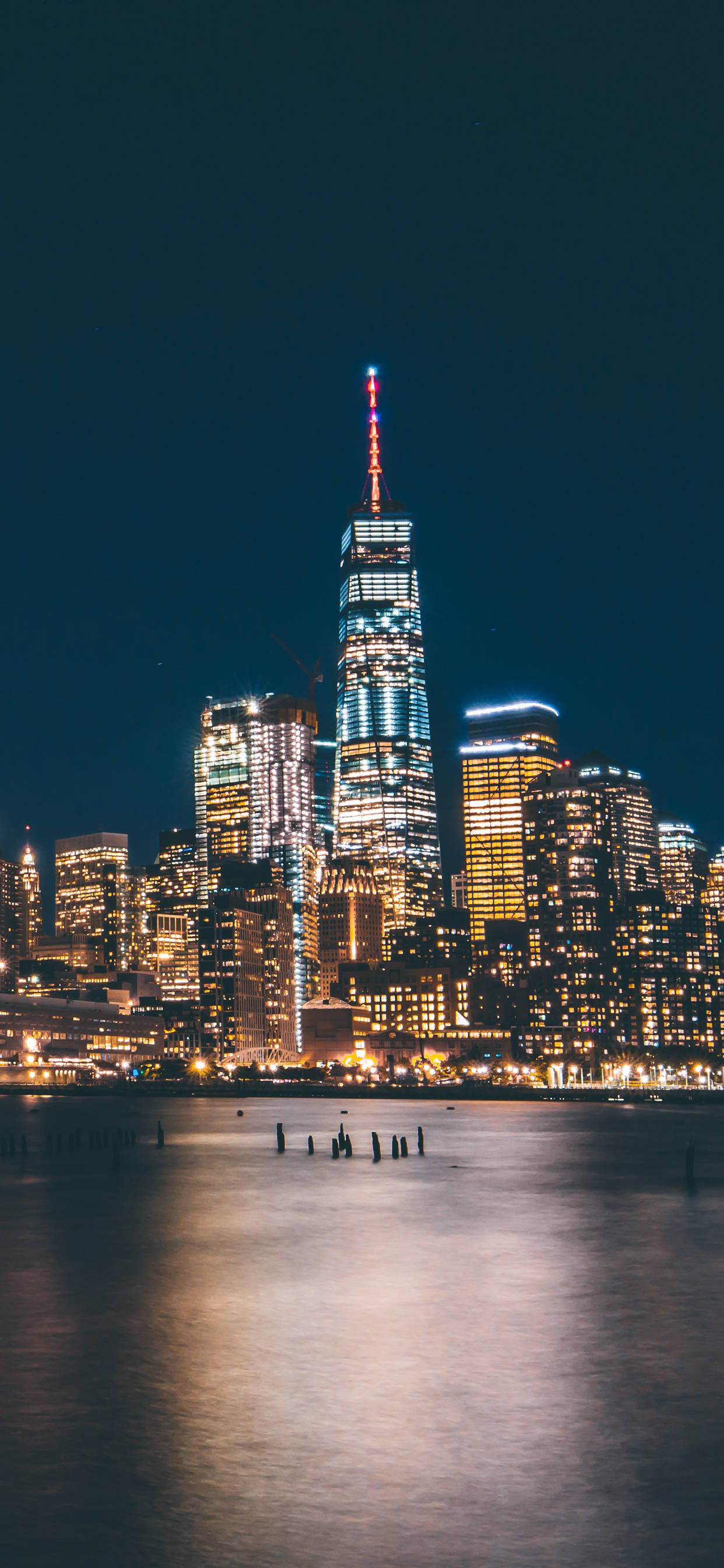 紐約 桌布 壁紙 — 令人驚嘆的夜景，照亮了世界貿易中心一號大樓及周圍摩天大樓，倒映在平靜的水面上。