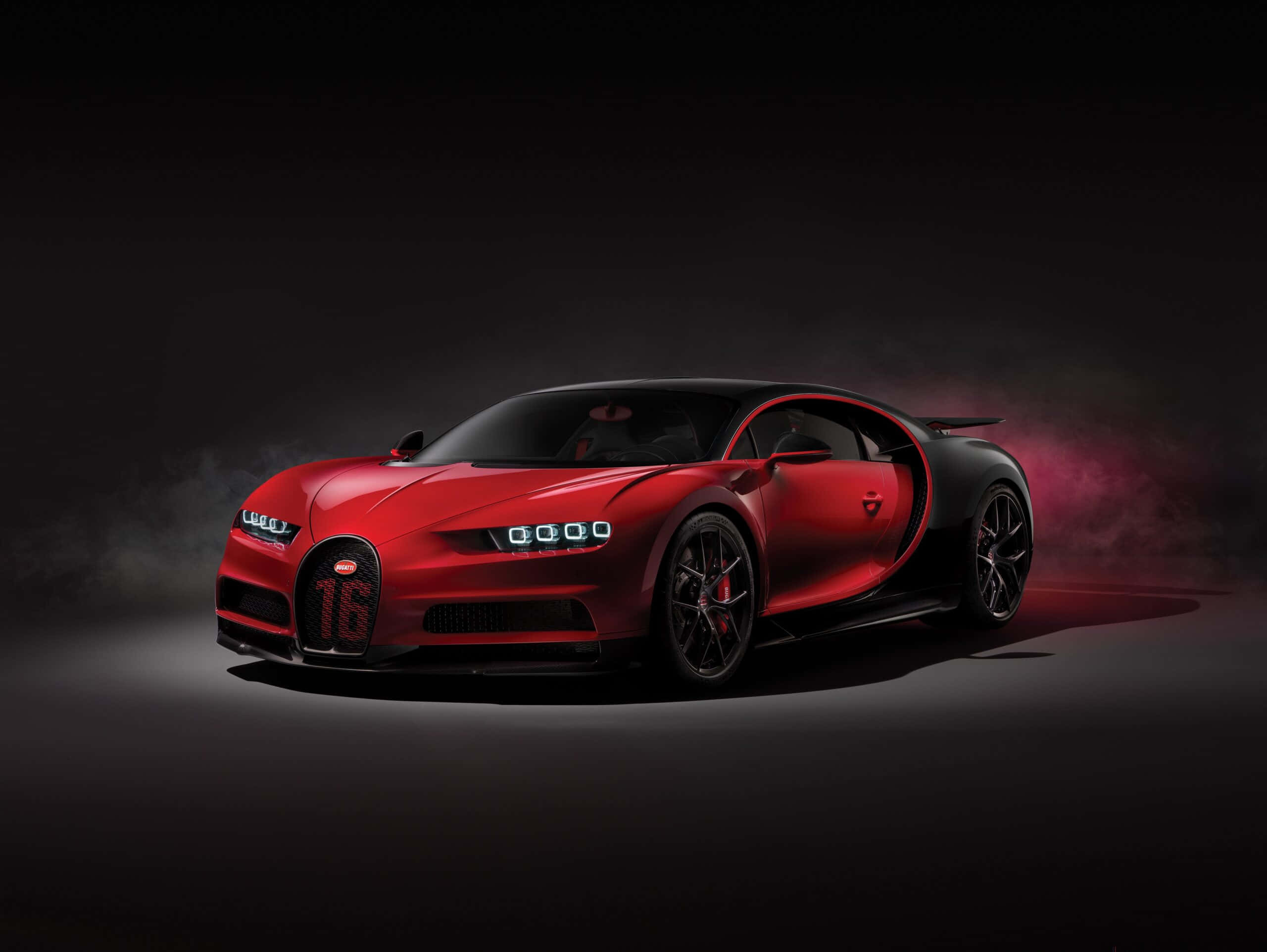 令人驚嘆的布加迪超跑 壁紙 — 一輛引人注目的紅色Bugatti Chiron，帶有黑色飾件和發光的車頭燈，戲劇性地站在黑暗煙霧背景前。