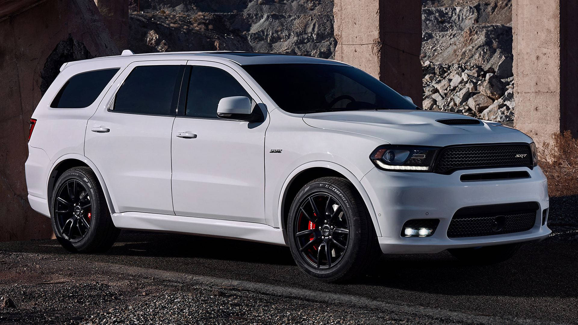 令人驚嘆的白色杜蘭戈 壁紙 — 一架時尚的白色Dodge Durango SRT停泊在混凝土柱下，背景有崎嶇岩石。