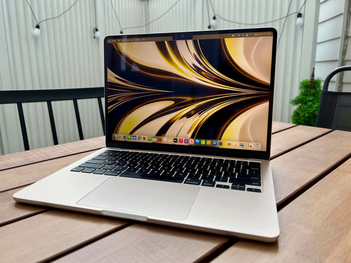 令人驚嘆的設計——MacBook 壁紙 — 一部銀色手提電腦，顯示著旋轉的金色和黑色牆紙，打開放在木製露台桌上，上方有燈串。