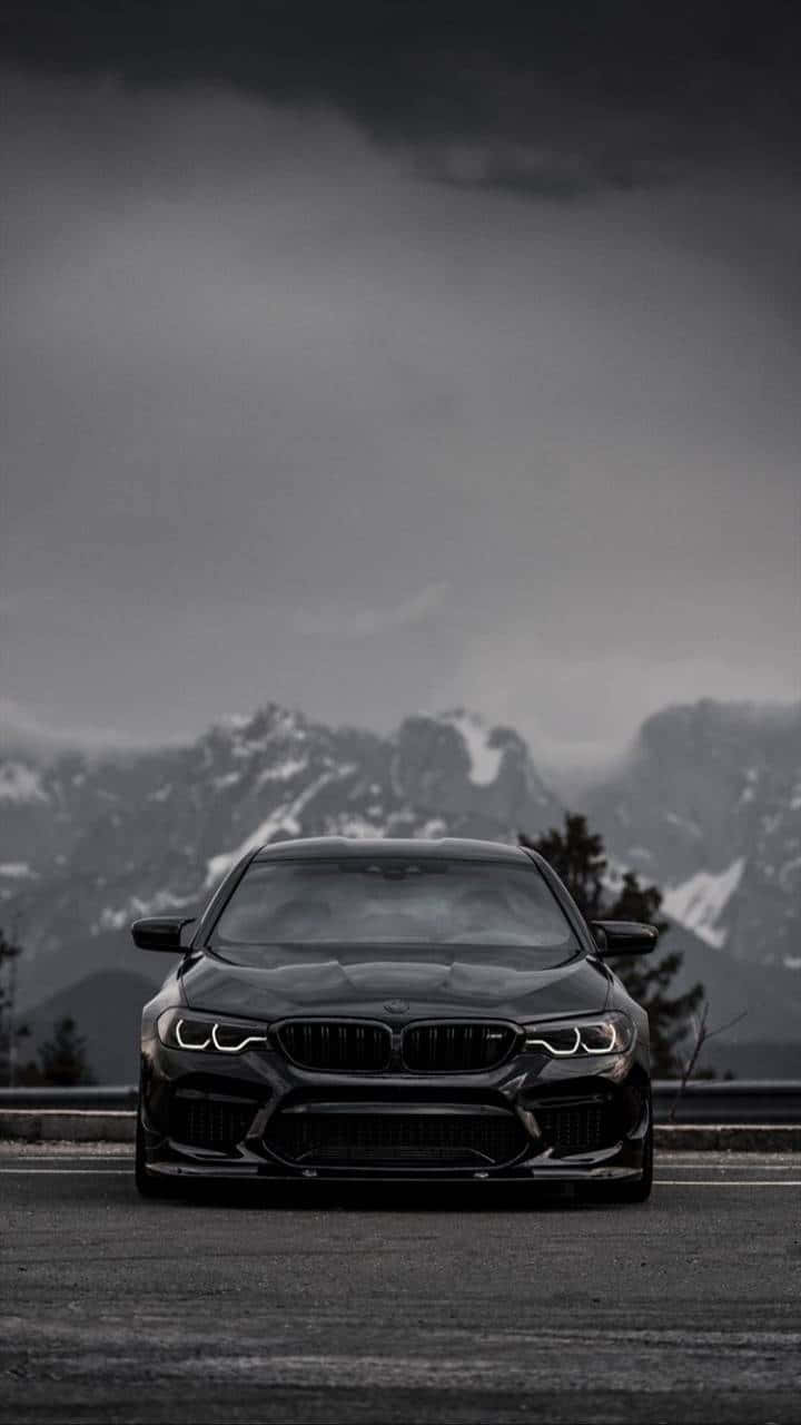 黑色BMW M5停在山路上，背景有白雪覆蓋的山峰和風暴般的天空。