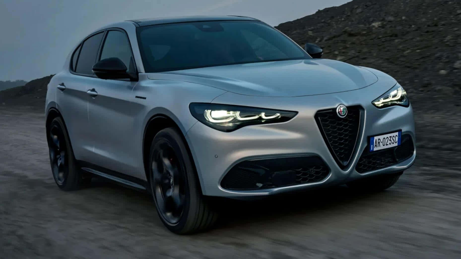 令人驚豔的Alfa Romeo 4C Spider敞篷跑車 壁紙 — 一輛時尚的銀色愛快羅密歐SUV在碎石路上行駛，背景是崎嶇的山丘，天空柔和。