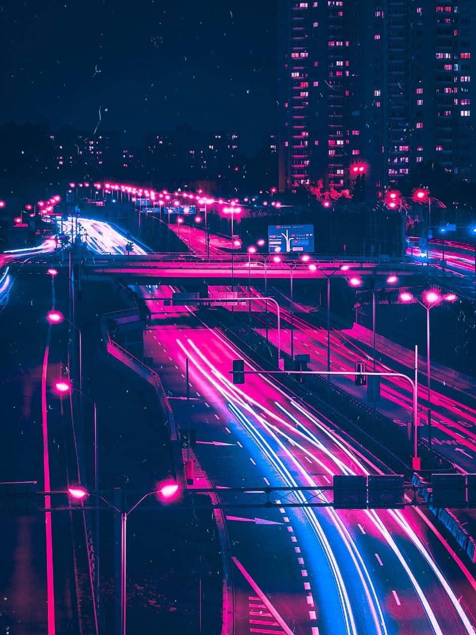 夜晚城市高速公路上汽車留下的霓虹粉紅和藍色光跡。