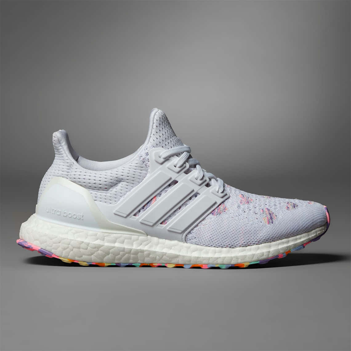 以 Adidas 達成個人最佳表現 壁紙 — 一雙白色Adidas Ultra Boost運動鞋，鞋底和鞋面帶有彩色斑點裝飾，背景為中性灰色。