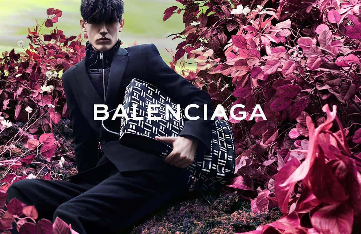 身穿黑色西裝的男子手持 Balenciaga 手袋，被洋紅色樹葉包圍。