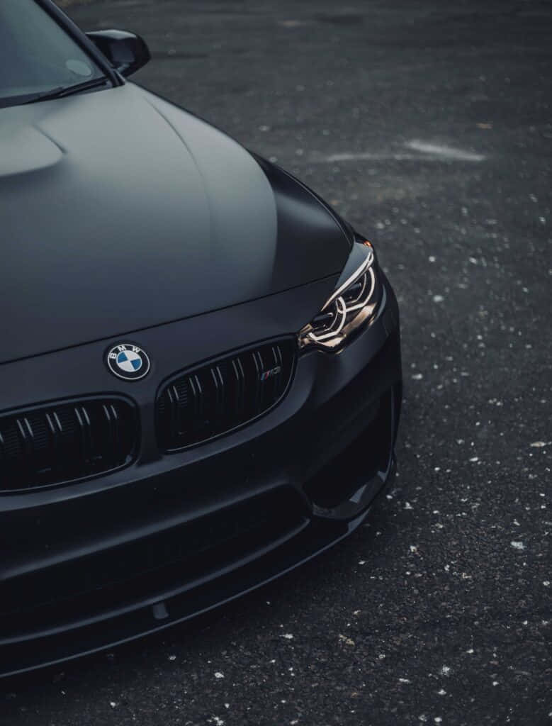 啞光黑色BMW M2跑車停在瀝青路上，帶有發光的頭燈。