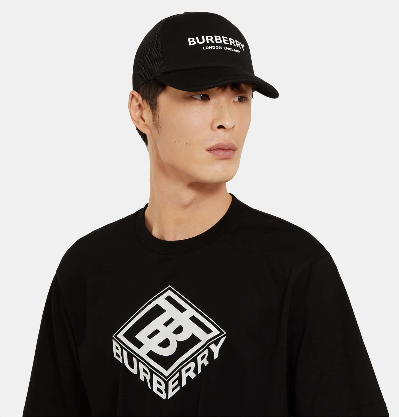以 Burberry 穿出時尚品味 壁紙 — 一名戴著黑色Burberry帽及配襯白色標誌T恤的男子站在純色背景前。