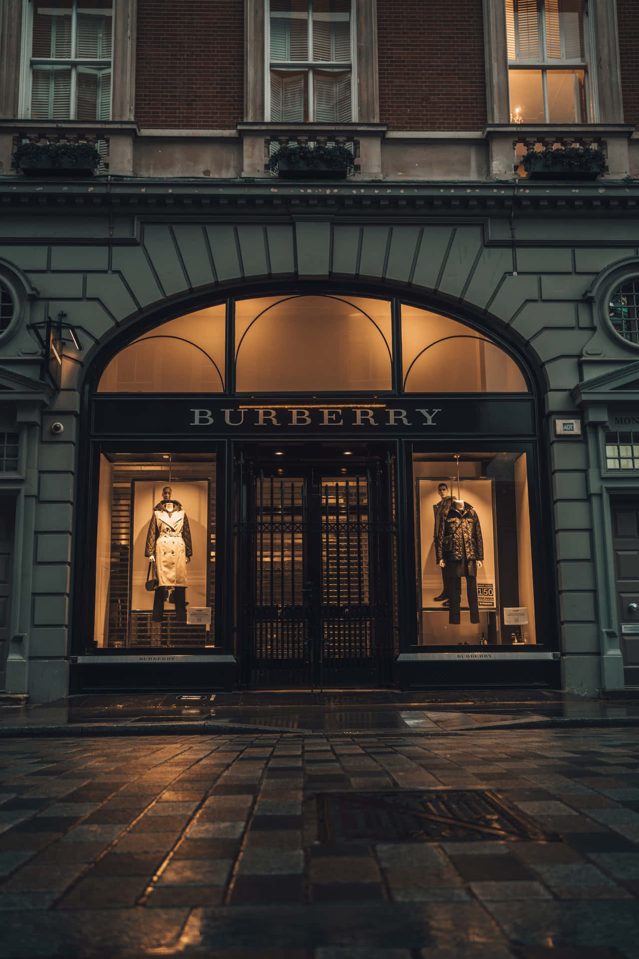Burberry 店舖正面，穿著風衣的人體模型在黃昏時在濕漉漉的鵝卵石上發光。