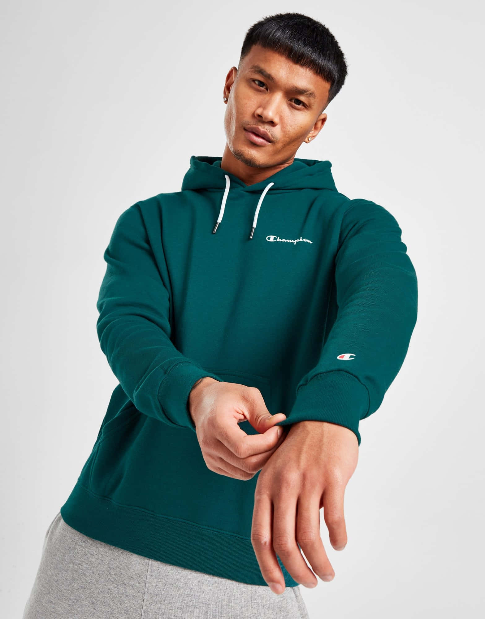 以 Champion 裝備提升你的表現 壁紙 — 一名身穿深綠色Champion連帽衫的男子在純白色背景前調整袖子。