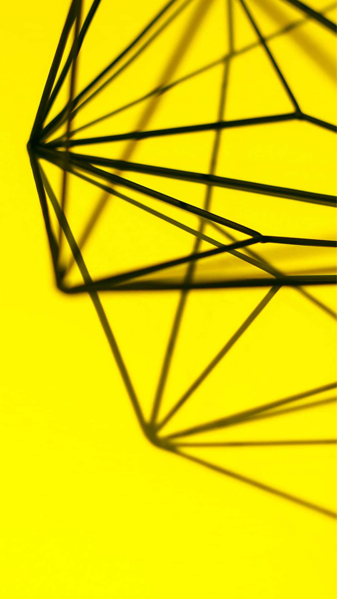 以 Design Simple iPhone 讓您的設備展現完美造型 壁紙 — 一個大膽的幾何線框結構在充滿活力的黃色背景上投下銳利的黑色陰影。