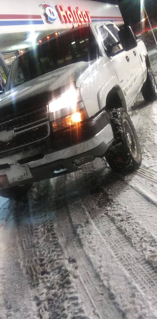 白色升高嘅貨車喺夜晚嘅加油站雪中行駛。