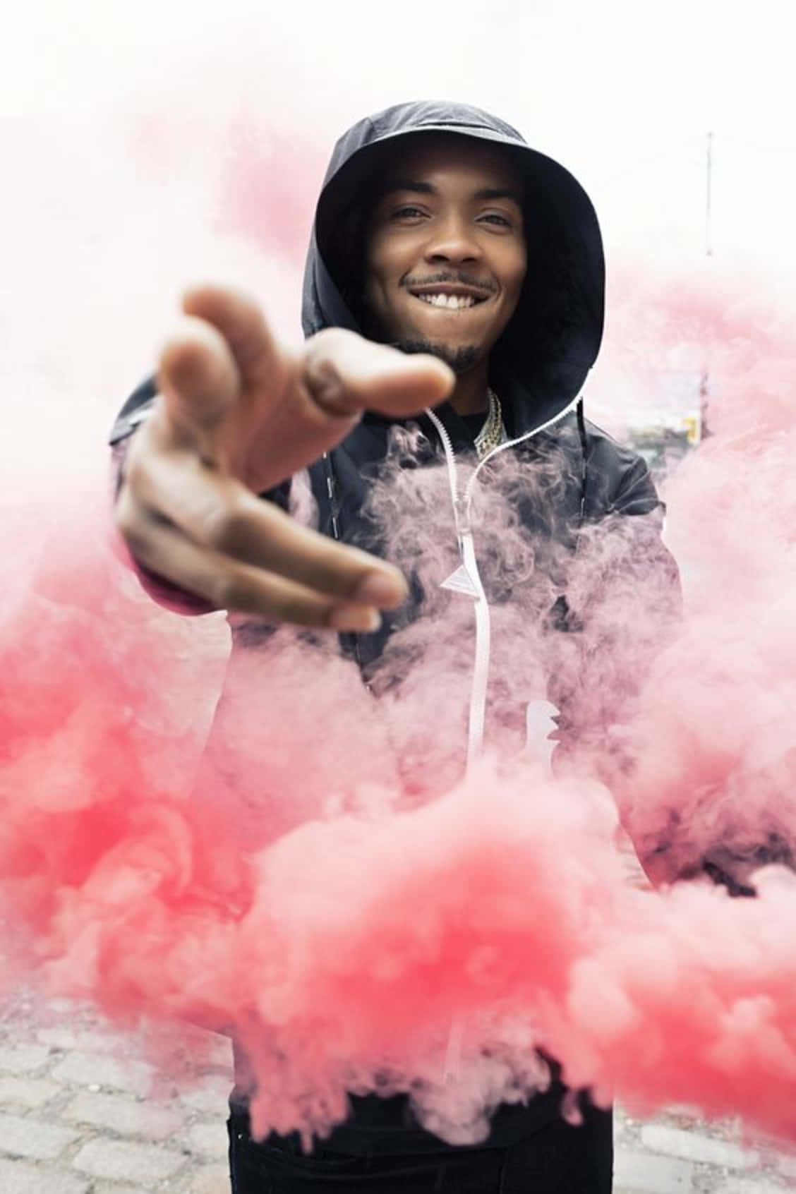 穿連帽衫的男人微笑著在城市的行人道上伸手穿過粉紅色煙霧
