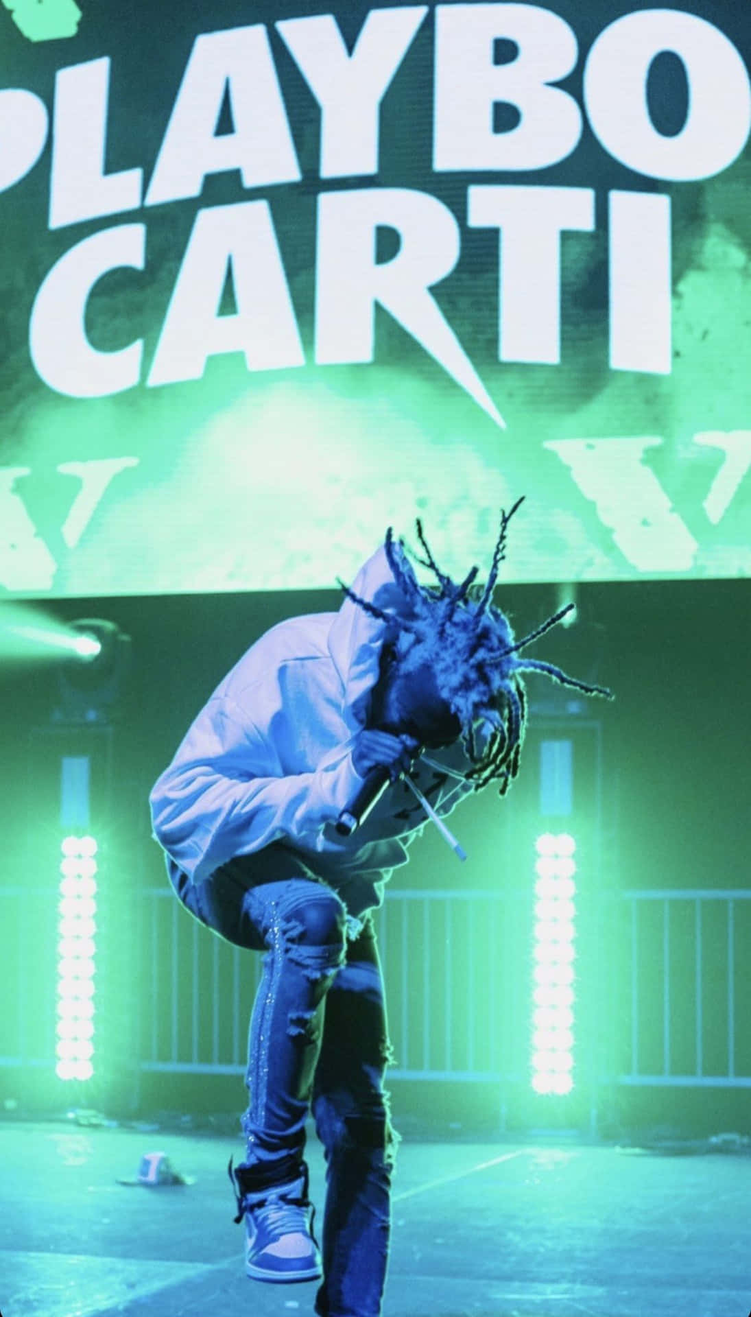 說唱歌手 Playboi Carti 在綠色燈光的舞台上表演，身後有大型文字。