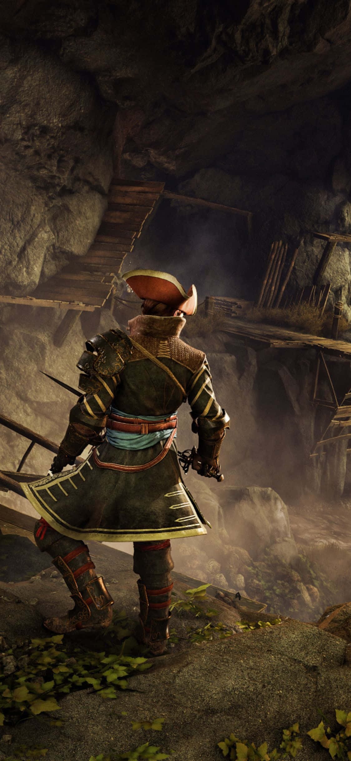 以 iPhone X 探索《Greedfall》的繁茂世界 壁紙 — 一位身穿精細盔甲的武士站在長滿青苔的懸崖邊緣，俯瞰著一個帶有木結構的迷霧洞穴。