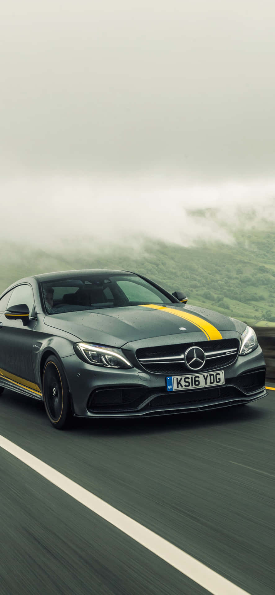 灰色 Mercedes-AMG 帶有黃色條紋在霧氣瀰漫的山路上行駛。