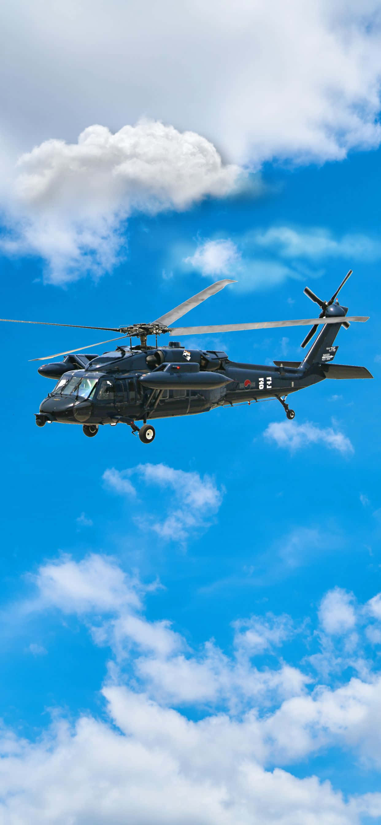 以 iPhone XS Max Helicopters 率領潮流 壁紙 — 一架黑色軍用直升機在點綴著蓬鬆白雲的明亮藍天中翱翔。