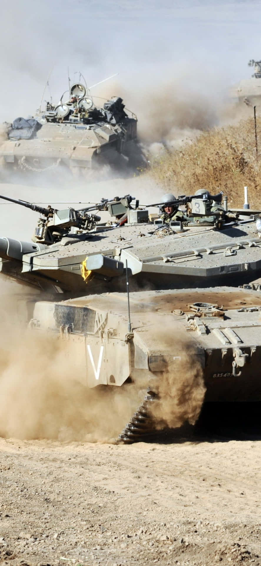 軍用坦克在塵土飛揚的沙漠戰場上行進。