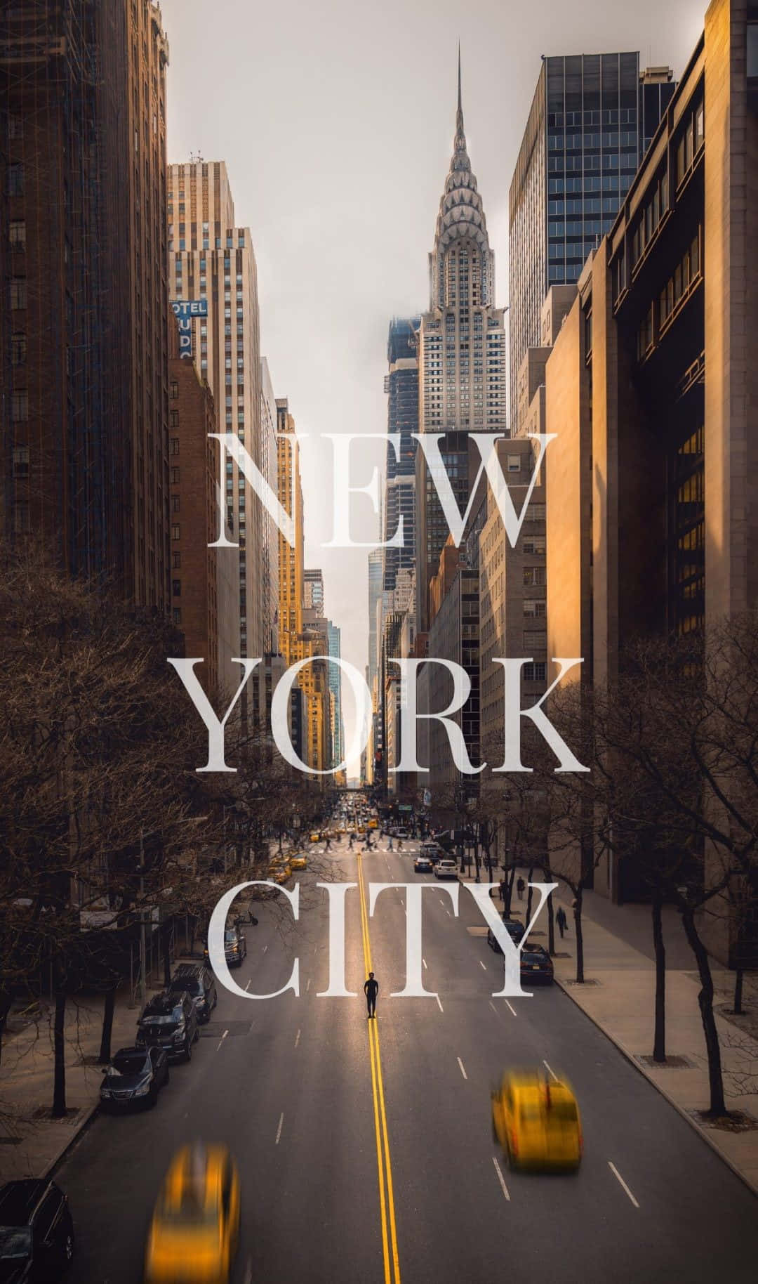 以 iPhone Xs 欣賞紐約市天際線的壯麗景色 壁紙 — 一個孤獨的行人走在陽光明媚的紐約市街道上，兩旁是高聳的摩天大樓和黃色的出租車。