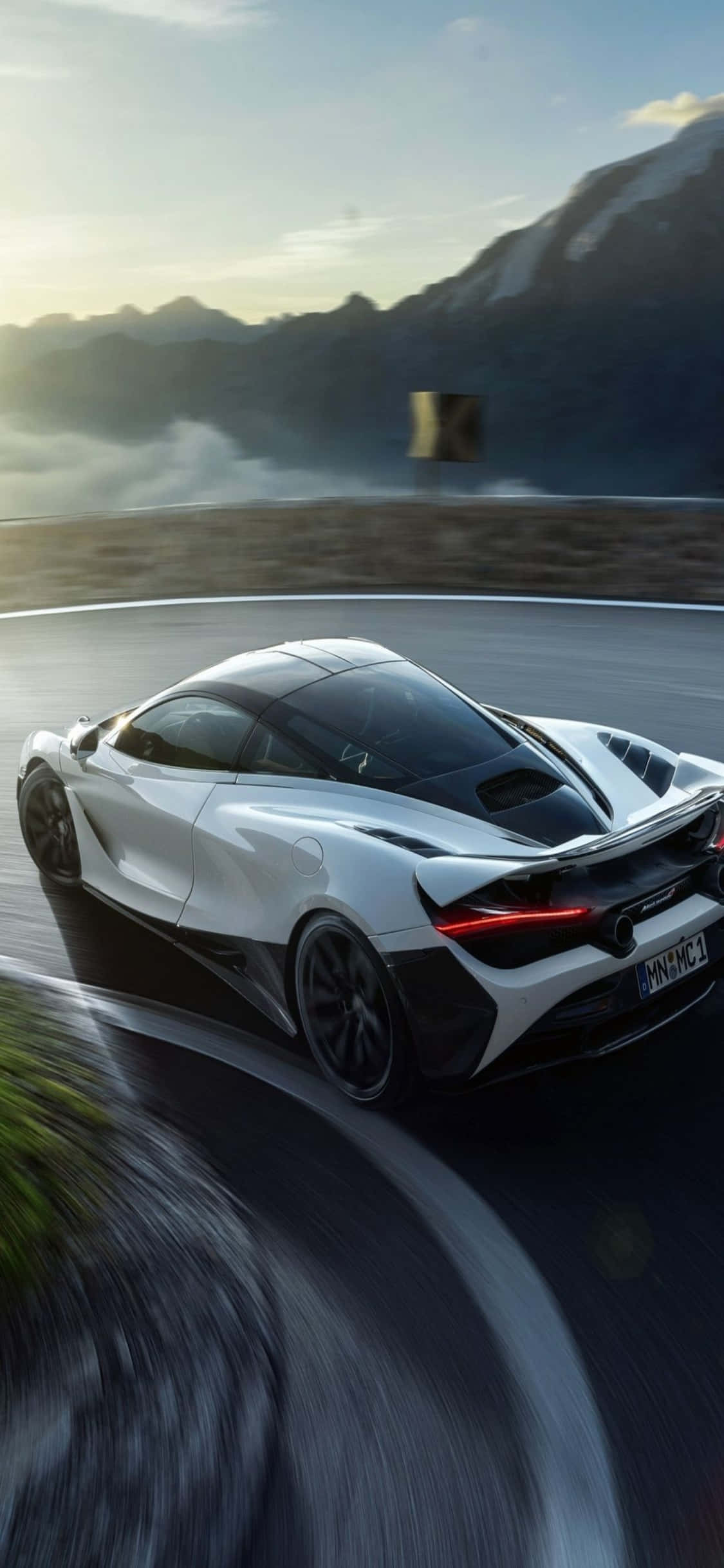 以 iPhone Xs 與 McLaren 720s 超越生活極限 壁紙 — 一輛白色McLaren跑車沿著蜿蜒的山路疾馳，背景是模糊的動感和霧氣繚繞的山峰。