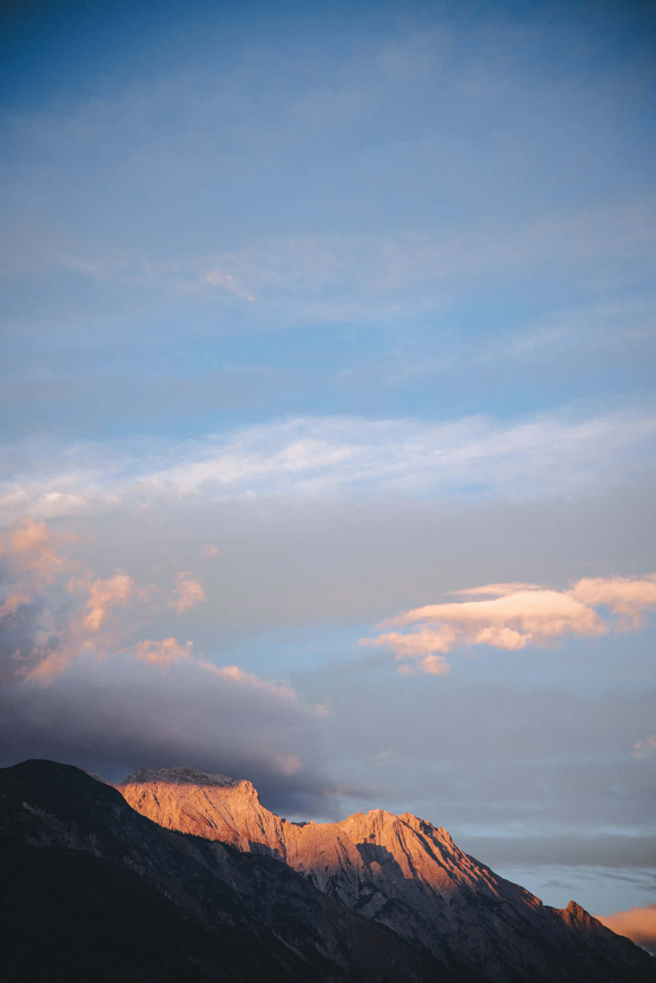 山峰在夕陽光中閃耀，伴隨柔和藍天與白雲。