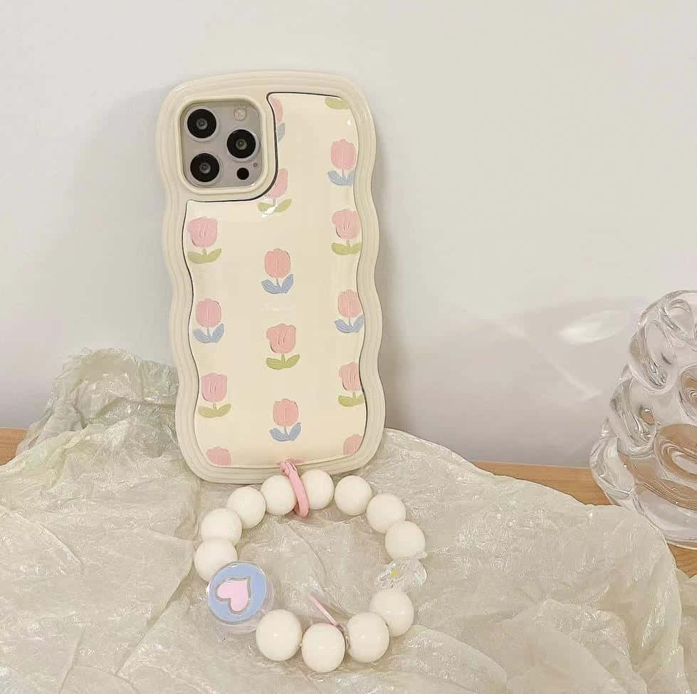 以 iPhone 捕捉的美麗日落 壁紙 — 一個粉彩鬱金香圖案的手機殼放在皺巴巴的塑膠上，旁邊有一個白色珠子手鍊和玻璃花瓶。