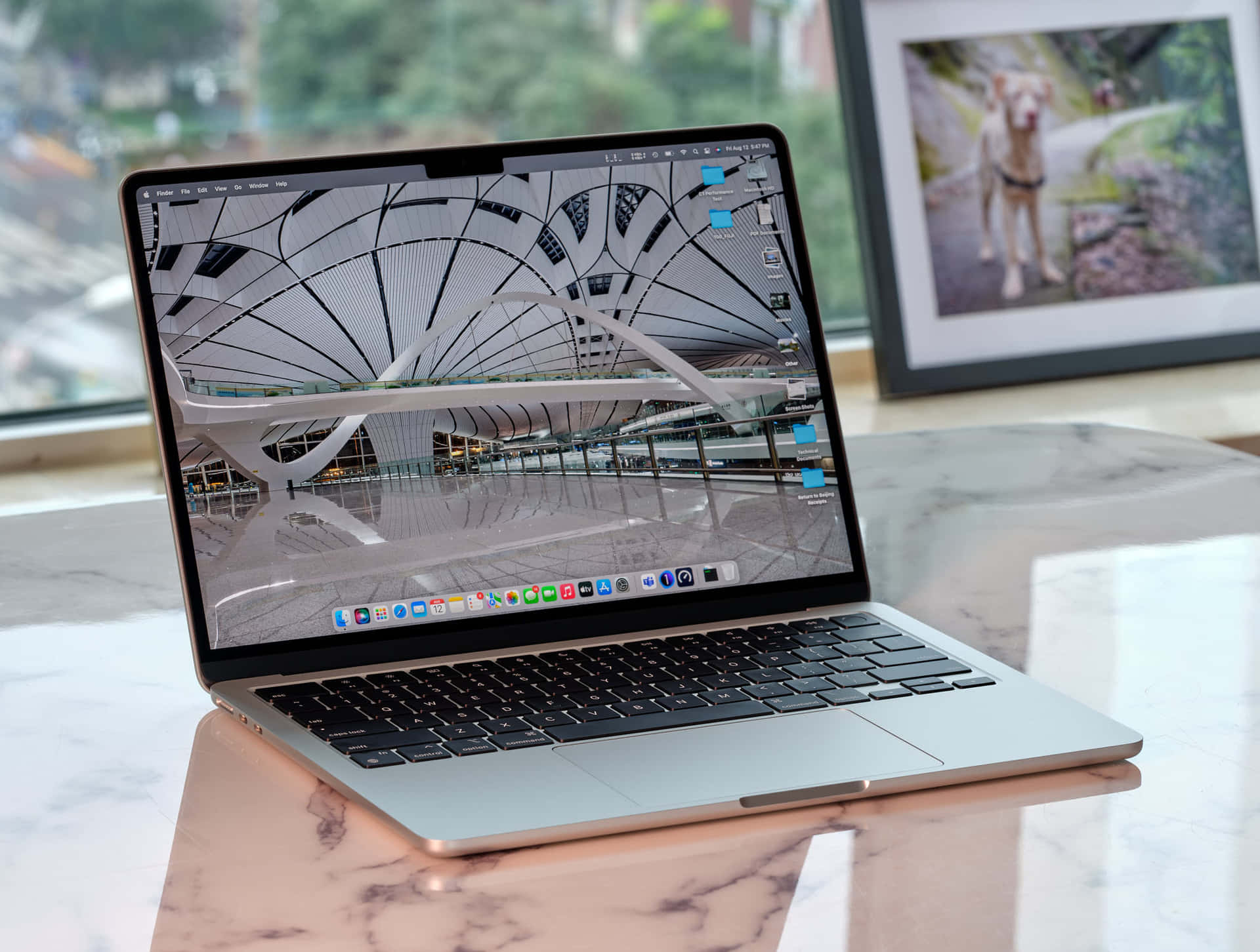 以 Macbook 激發你的創意靈感 壁紙 — 一部銀色手提電腦打開放在大理石桌上，顯示未來主義建築內部，有彎曲的白色橫樑和玻璃欄杆。